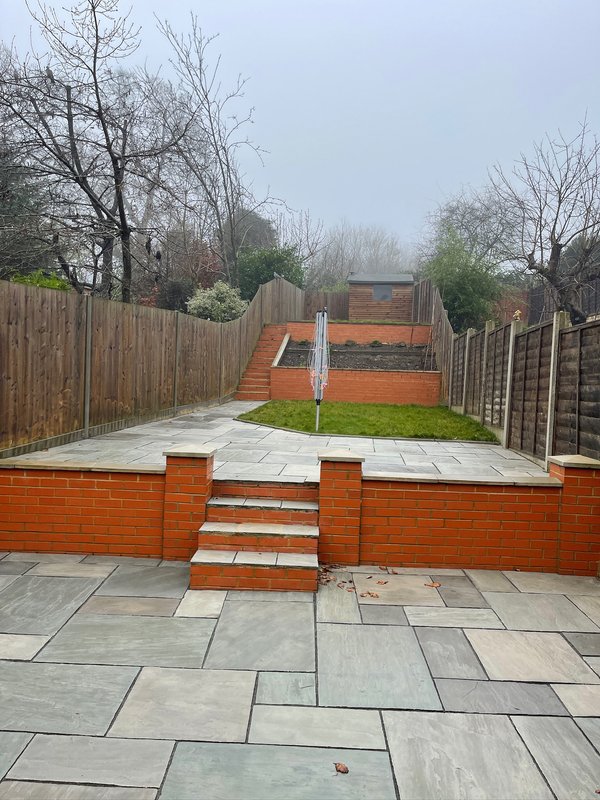 Modern garden with paved patio, brick raised beds, and wooden fence surrounding property