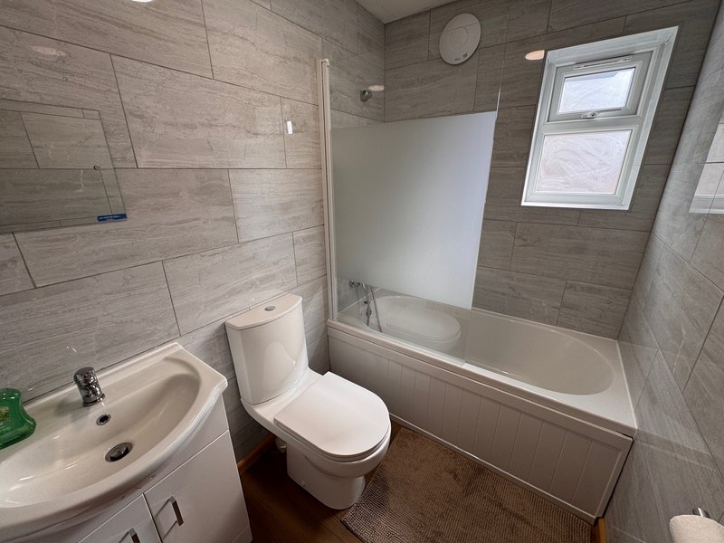 Modern bathroom with white toilet, sink, bathtub with shower enclosure and window