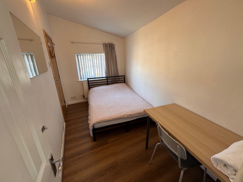 Bedroom with double bed, wooden desk, mirror and vertical blinds on window