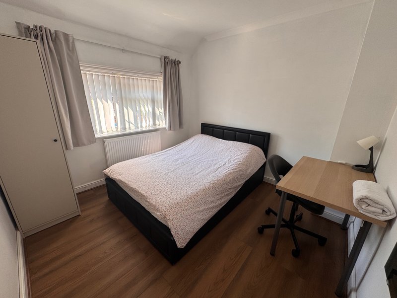 Bedroom with black bed frame, wooden desk, chair, window with curtains and radiator