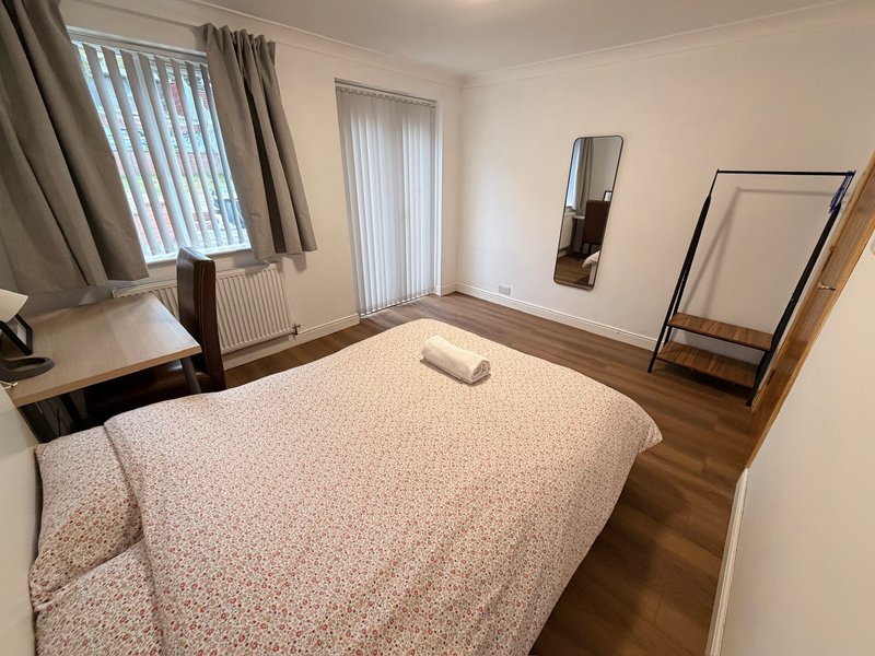 Bedroom with double bed, wooden floor, desk, mirrors and vertical blinds