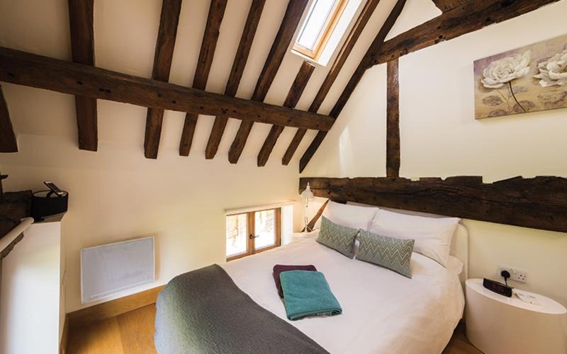 Bedroom with exposed wooden beams, double bed, green cushion and teal throw blanket