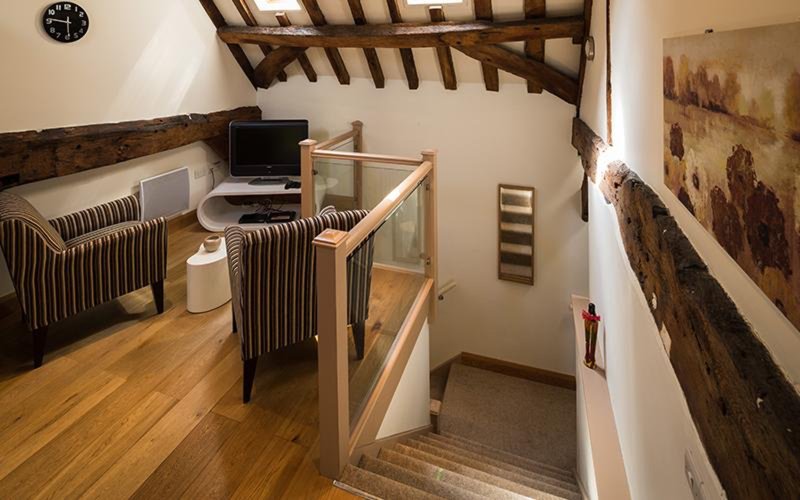 Loft bedroom with exposed wooden beams, wooden flooring, radiators and staircase
