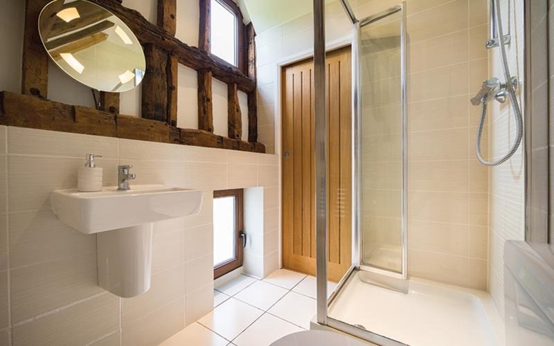 Modern bathroom with wall-mounted sink, round mirror, wooden shelving, and glass shower enclosure