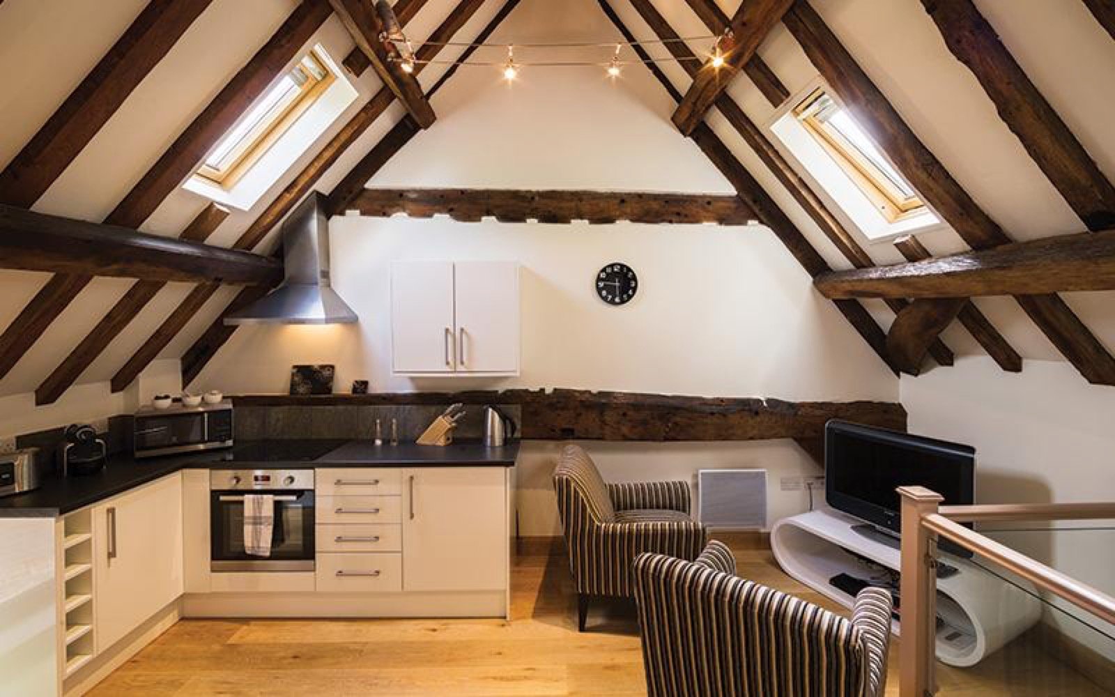 Modern attic kitchen with cream cabinetry, exposed beams, skylights and wooden flooring