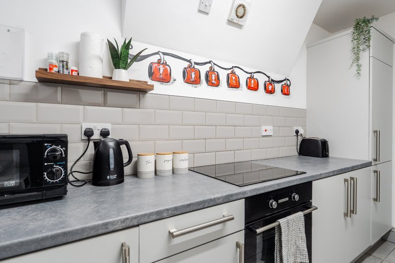 Modern kitchen with white cabinetry, grey countertop, black appliances and decorative orange lanterns
