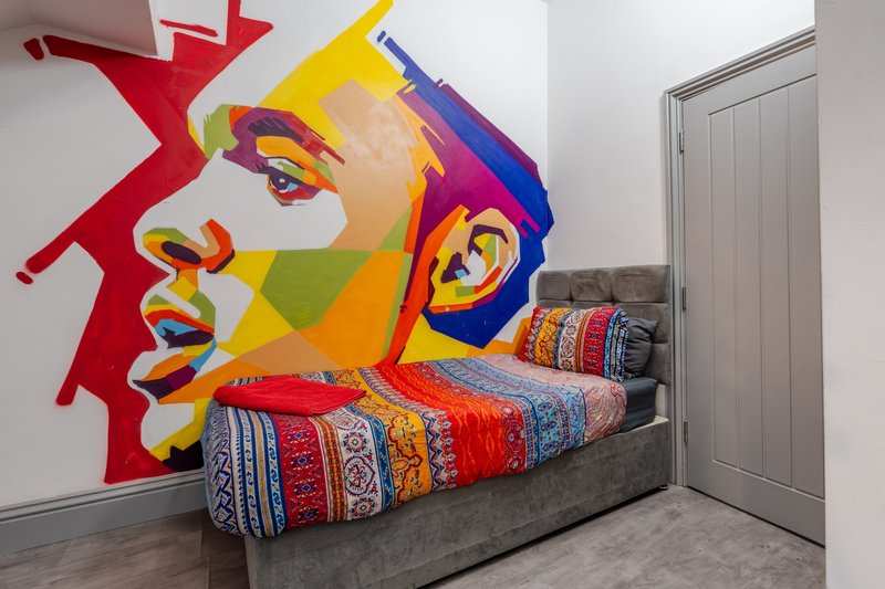 Bedroom with colorful pop-art mural on wall, patterned bedding, and gray bed frame