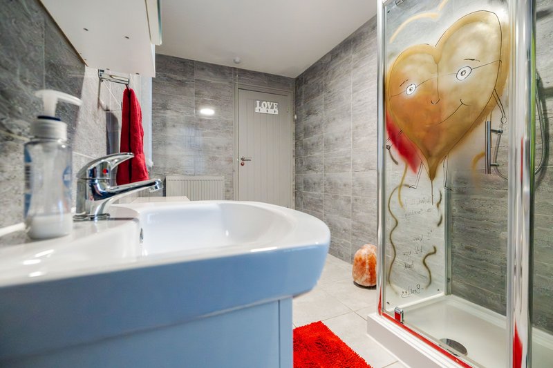 Modern bathroom with blue basin, grey tile walls, shower enclosure and red accents
