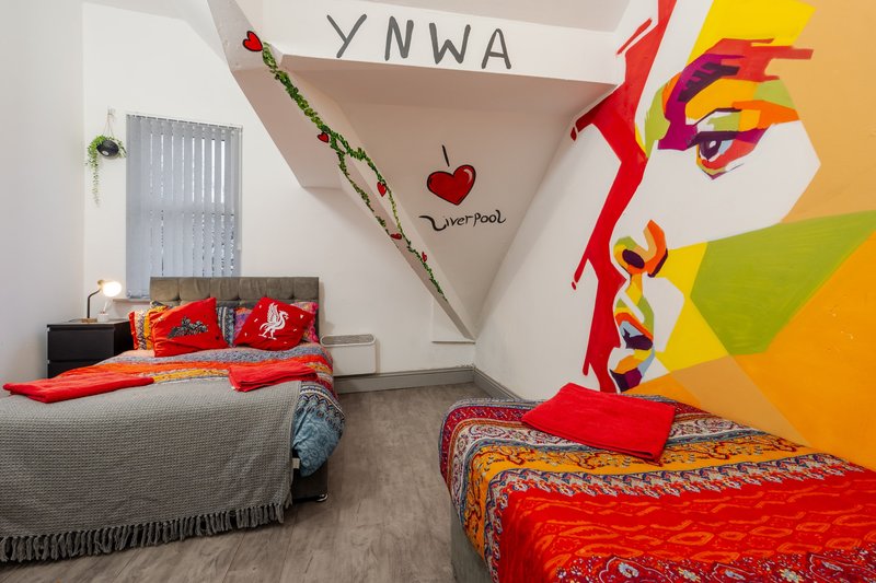 Colorful bedroom with two beds, vibrant wall art, decorative branches and red accents