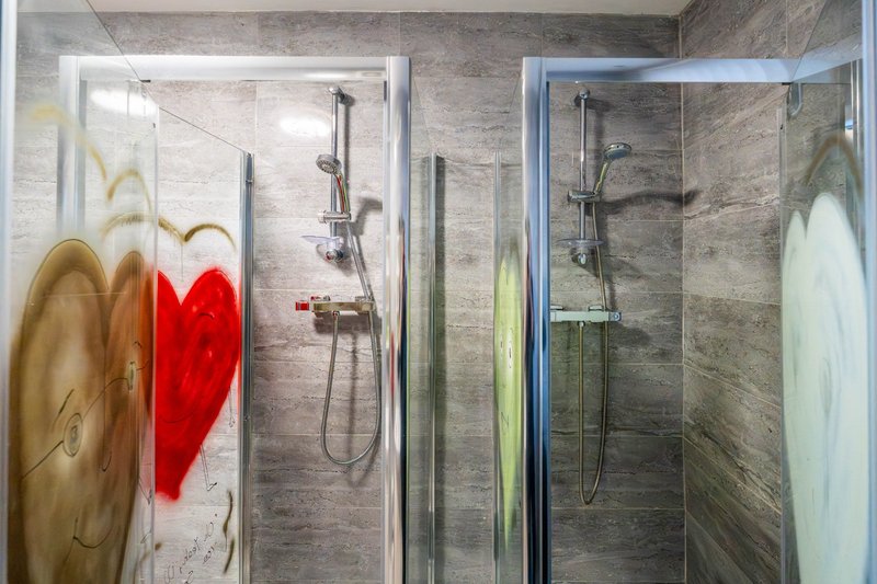 Modern bathroom with two walk-in showers, grey tile walls, and colorful towels