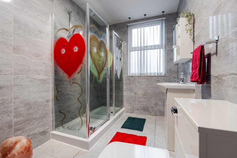 Modern bathroom with shower enclosure, white sink, tiled walls and red heart artwork