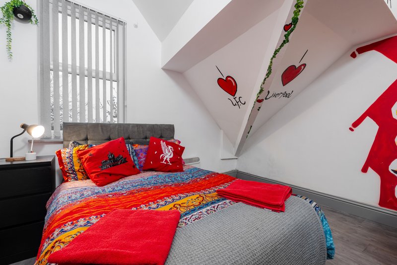 Bright bedroom with red and orange bedding, colorful pillows, and decorative wall art with apples