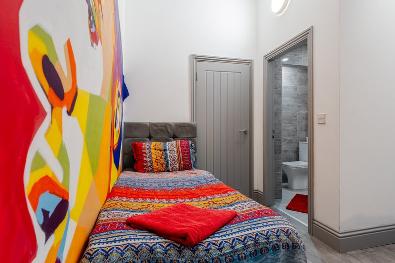 Colorful bedroom with single bed, patterned bedding, artwork on wall, and en-suite bathroom door