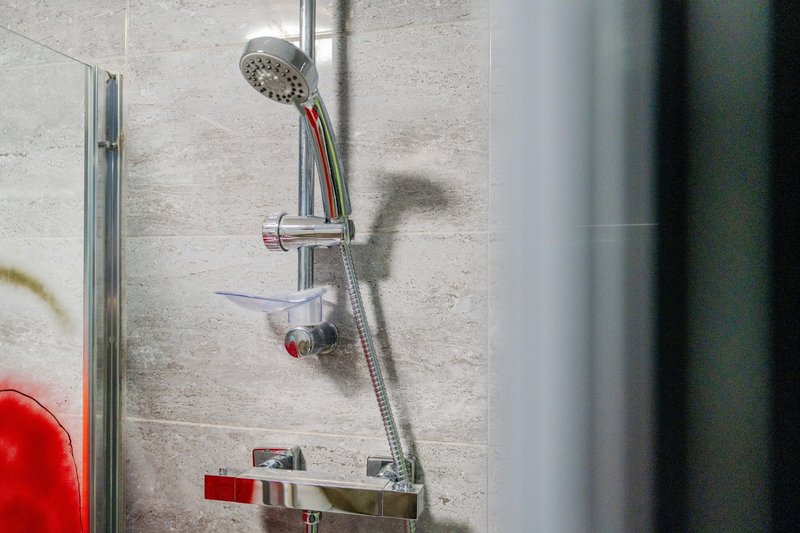 Bathroom shower fixture with handheld showerhead and chrome rail against tiled wall