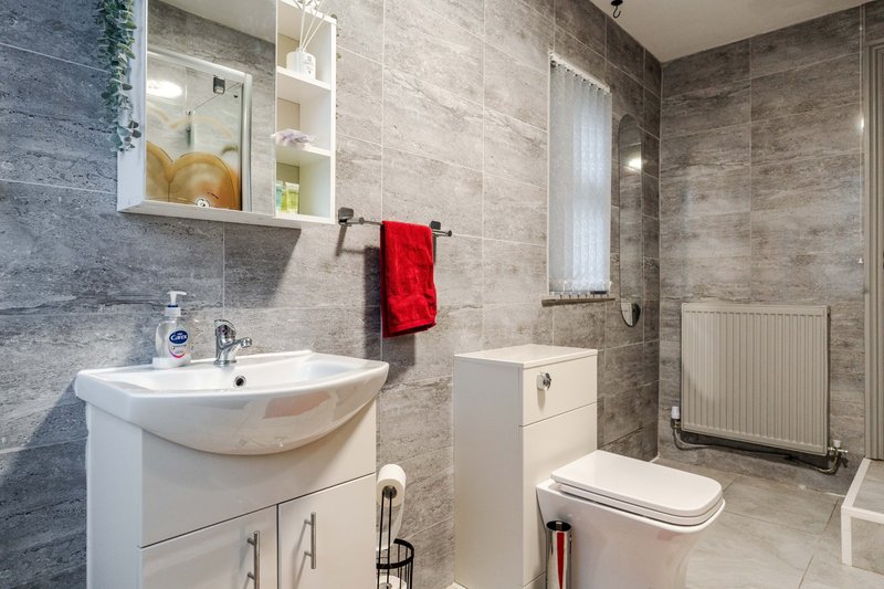 Modern bathroom with white sink vanity, toilet, radiator and tiled walls