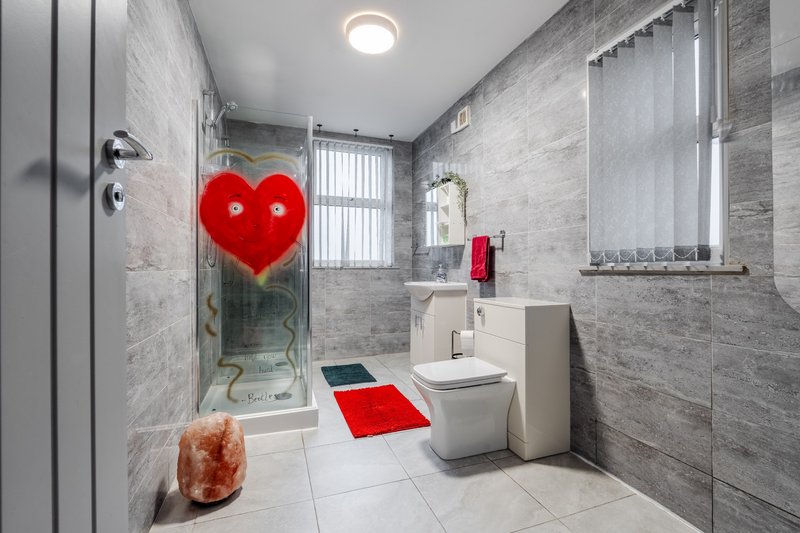 Modern bathroom with walk-in shower, toilet, sink, and decorative red heart and bath mat