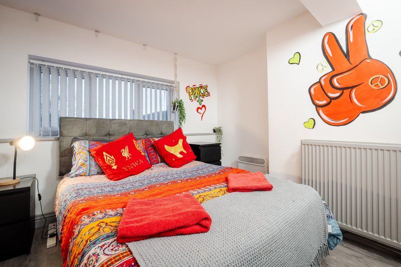 Bright bedroom with double bed, red bedding, orange wall decal, and vertical blinds