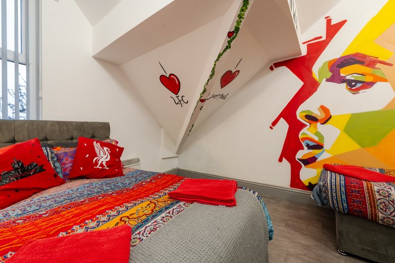 Attic bedroom with red bedding, colorful wall art, and sloped ceiling with pendant light