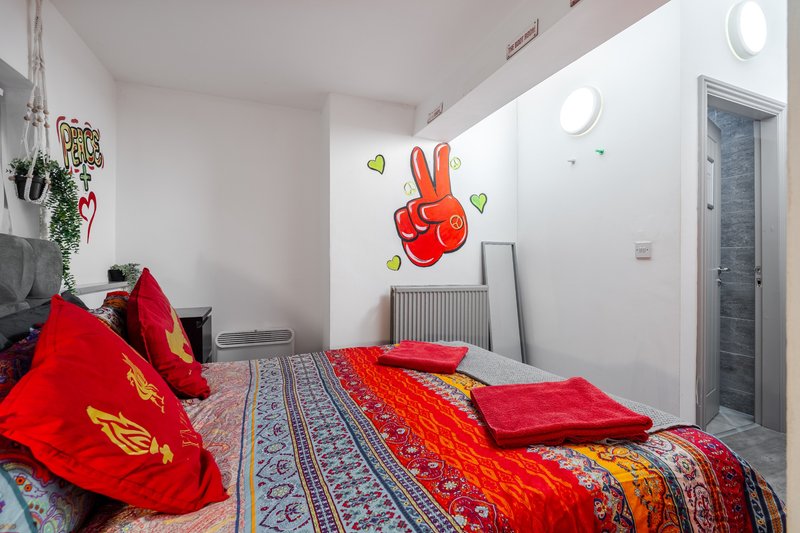 Bright bedroom with red bedding, patterned rug, wall art, and decorative plants