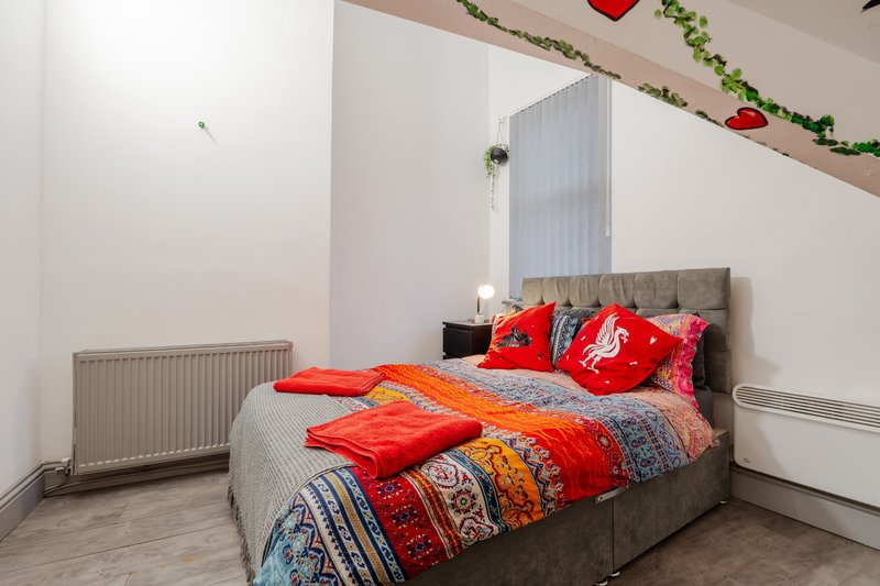 Bedroom with gray upholstered bed, red and orange bedding, radiator, and festive ceiling garland