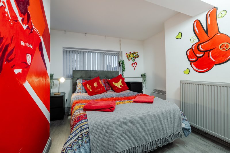 Bright bedroom with double bed, red bedding, wall art, and vertical blinds