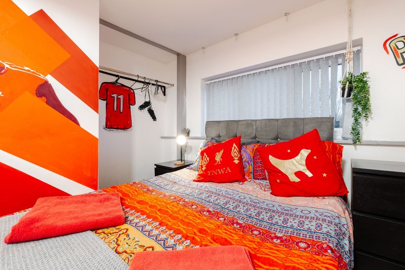 Bedroom with red and orange bedding, colorful wall art, plants, and natural light from windows