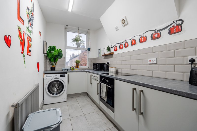 Modern kitchen with white cabinets, black countertop, washing machine, and decorative red wall art
