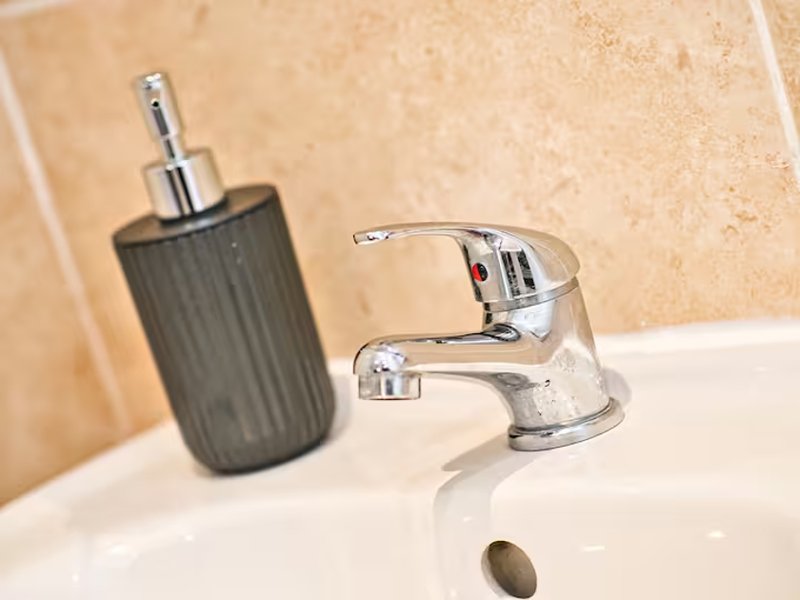 Bathroom sink with chrome faucet, soap dispenser and beige tile wall