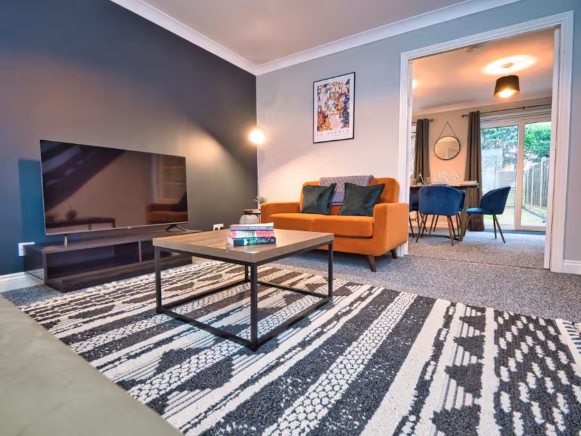 Modern living room with orange sofa, TV, wooden coffee table, patterned rug and blue armchairs