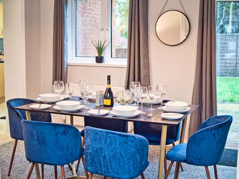 Dining room with blue velvet chairs, dark table, wine bottle, place settings and round mirror