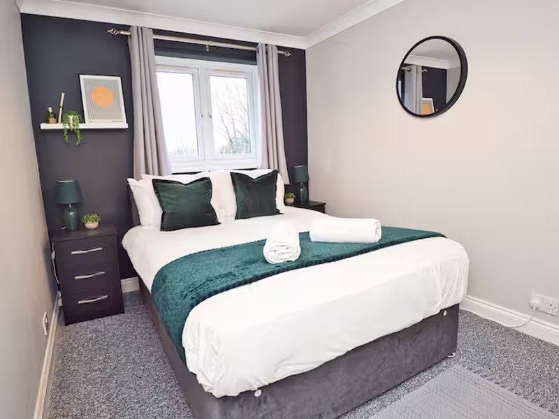 Modern bedroom with double bed, teal bedding, dark feature wall and round mirror