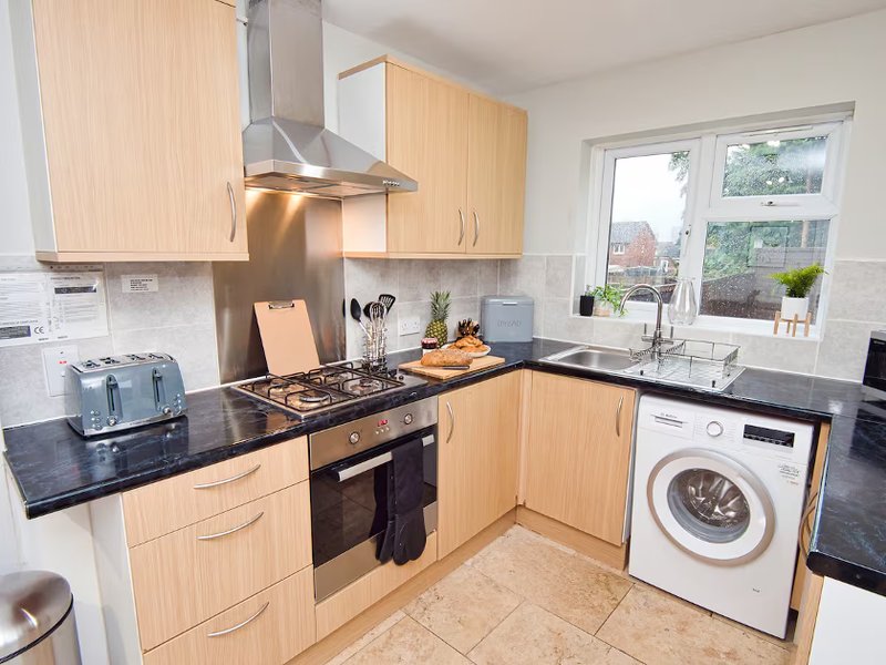 Modern kitchen with light wood cabinets, black countertops, gas hob, and integrated appliances