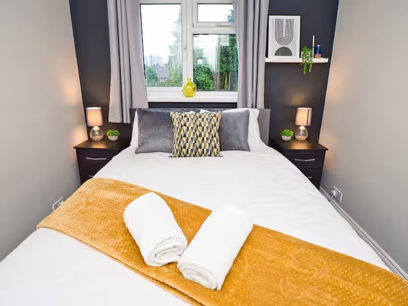 Modern bedroom with double bed, yellow throw, white towels, dark accent wall and window view