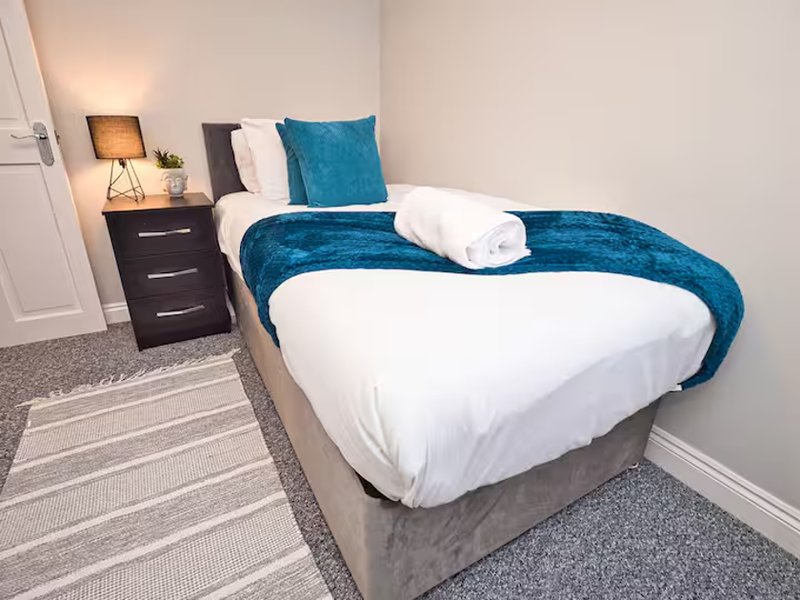 Modern bedroom with double bed, blue cushions, white bedding, dark nightstand and lamp