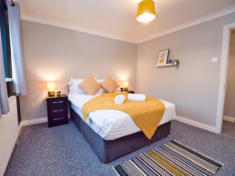 Bedroom with double bed, yellow bedding, bedside lamps, and striped rug