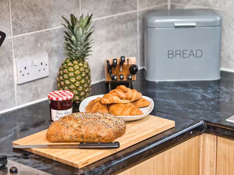 Kitchen countertop with fresh bread, croissants, pineapple and bread bin