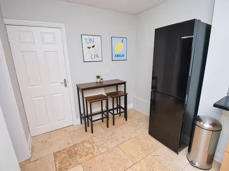 Kitchen area with black refrigerator, dining table, two stools, and framed wall art