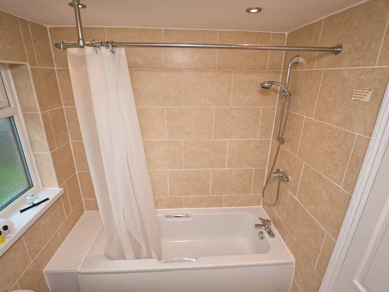 Bathroom with beige tile walls, white bathtub, shower curtain and chrome fixtures