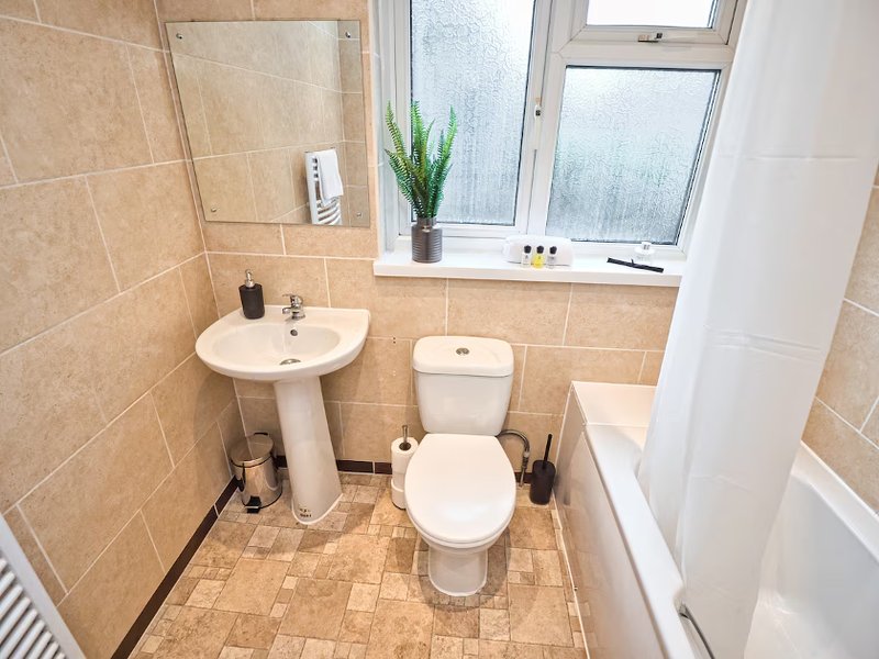 Bathroom with pedestal sink, toilet, window, and beige tile walls
