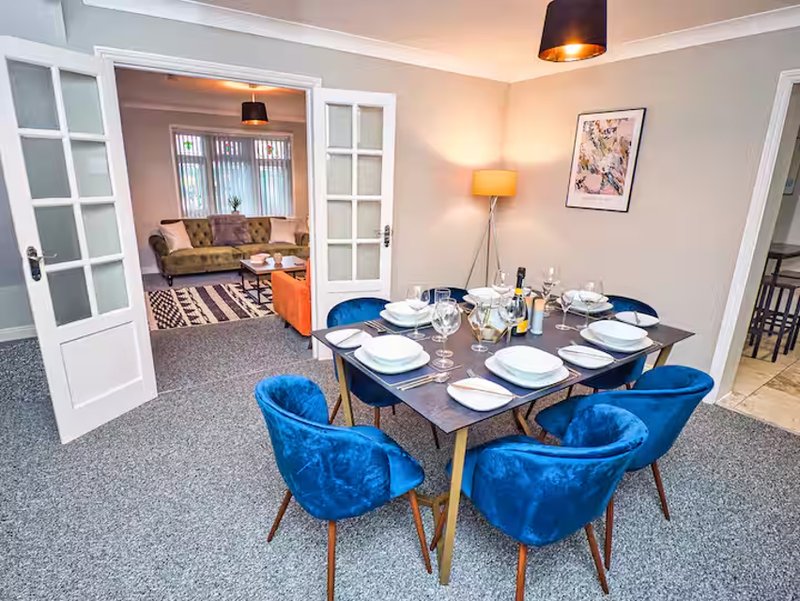 Dining room with blue chairs, set table, and living room visible through open doors