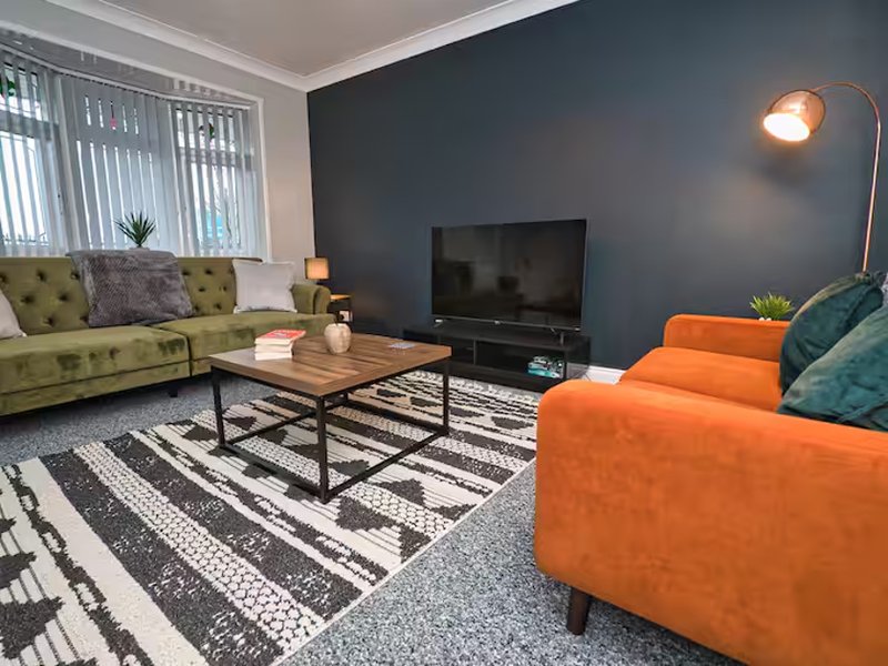 Modern living room with green and orange sofas, dark accent wall, TV, wooden table and geometric rug