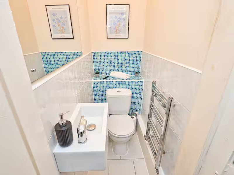 Small bathroom with white tiles, blue mosaic accent wall, toilet, sink and heated towel rail