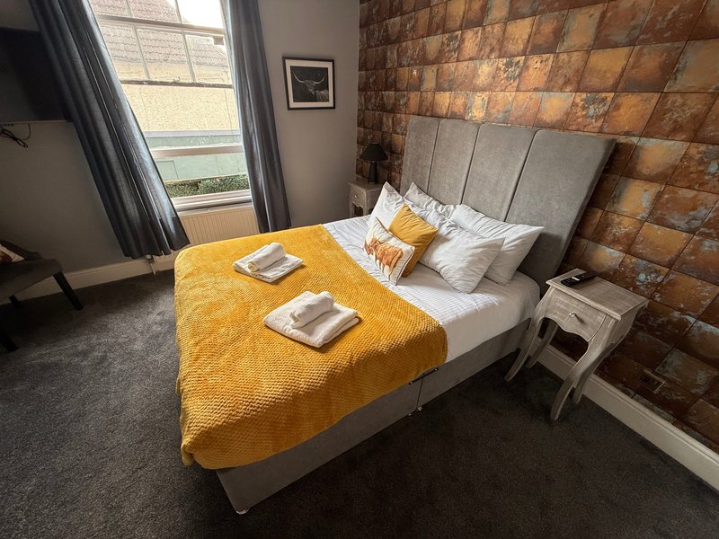 Bedroom with double bed, yellow throw, exposed brick wall and window