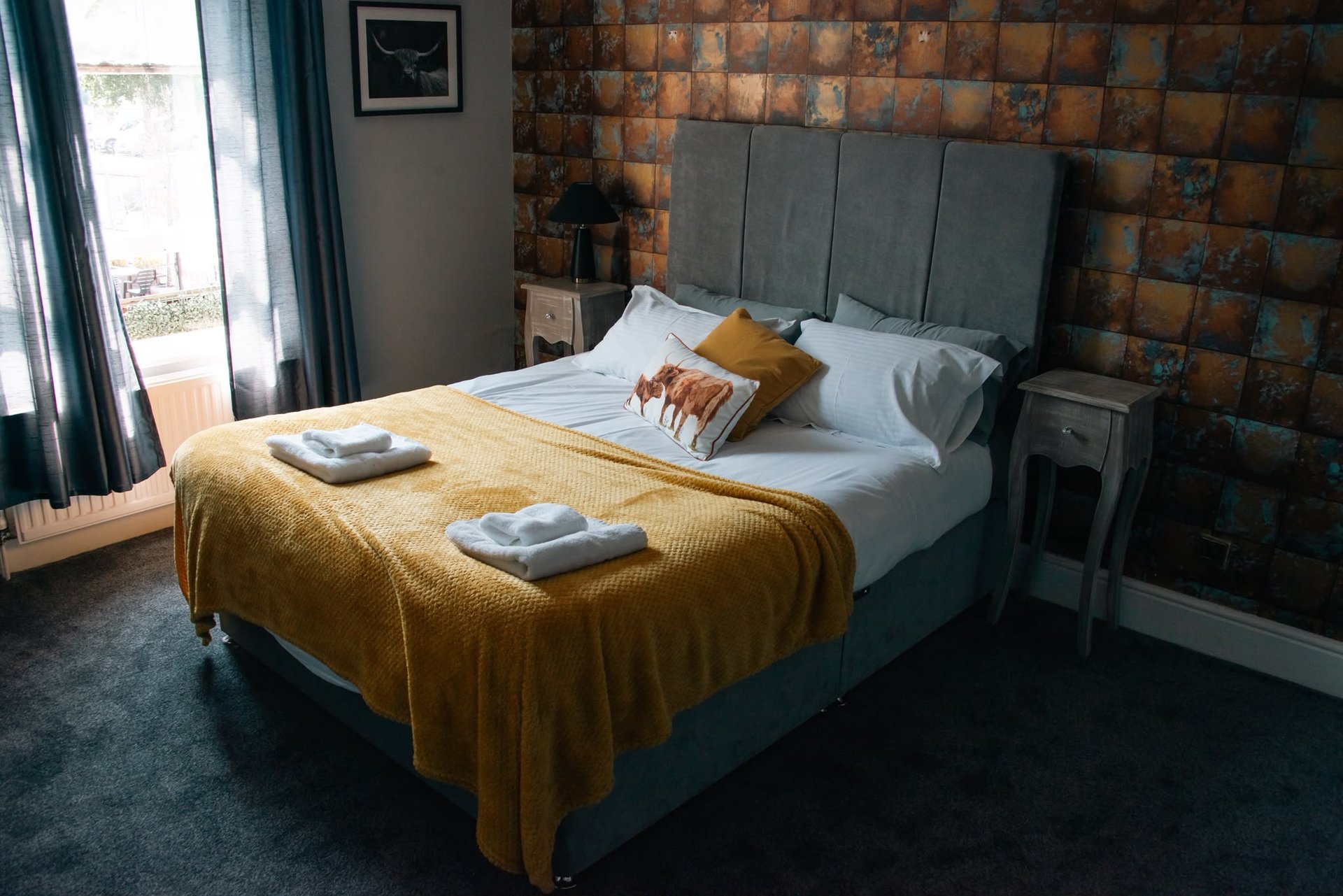 Bedroom with double bed, mustard throw, grey headboard, and exposed brick feature wall