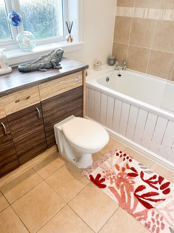 Bathroom with toilet, wooden vanity, bathtub, window and patterned floor mat