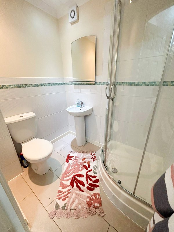 Clean bathroom with toilet, pedestal sink, shower enclosure and decorative floor mat