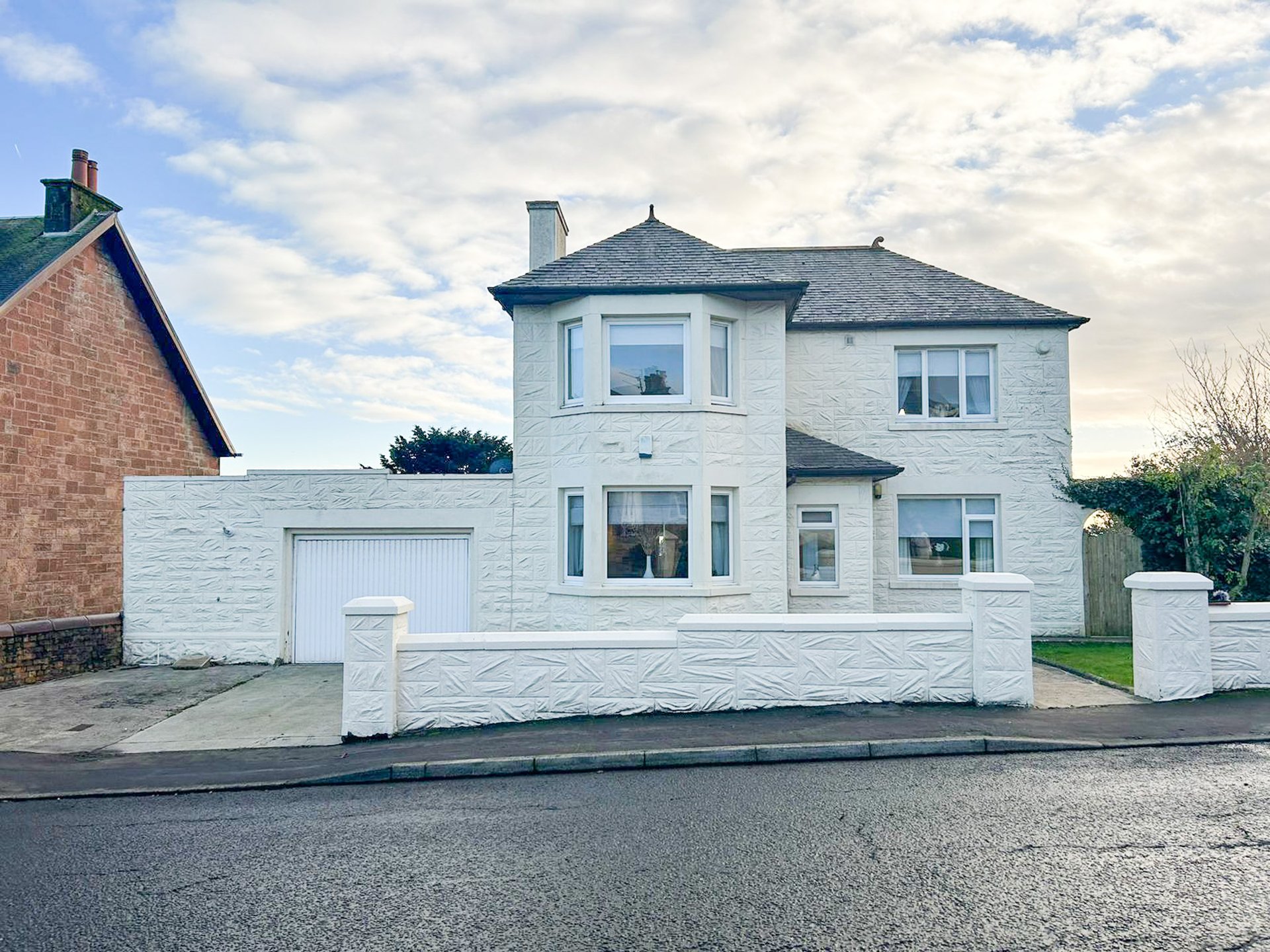 White two-story detached house with garage, driveway, and front garden wall