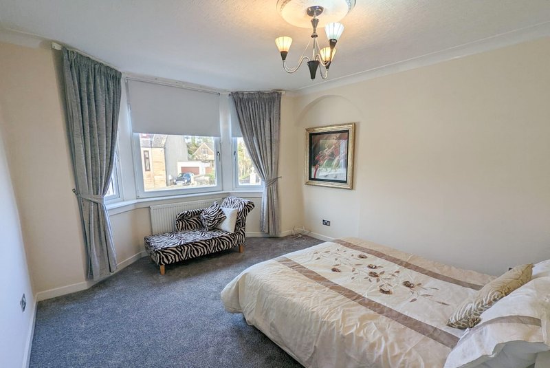 Bright bedroom with double bed, window seat, grey curtains and ceiling light fixture