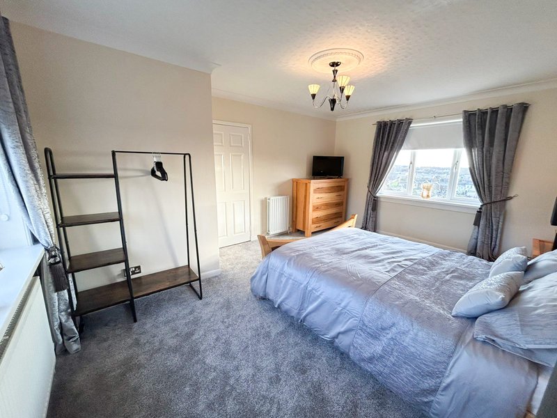 Spacious bedroom with double bed, wooden dresser, window with grey curtains and ceiling light