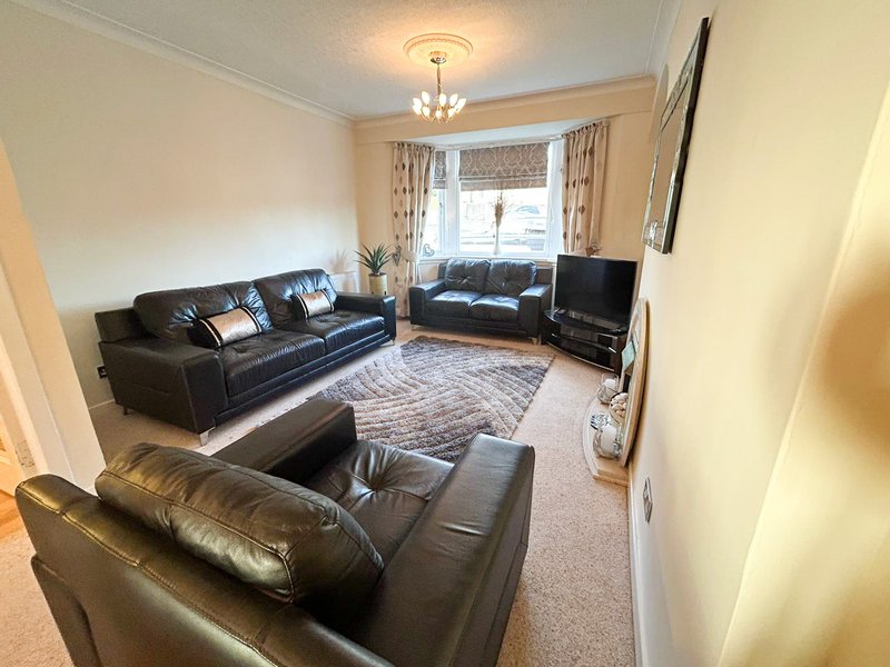 Spacious living room with three black leather sofas, TV, chandelier and bay windows